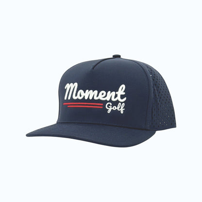 Moment Golf navy blue 5-panel performance hat with white embroidered script logo and laser-perforated side panels.