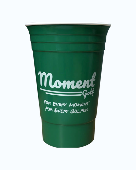 Moment Golf forest green reusable 16 oz party cup with white logo and text on a wooden surface