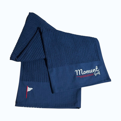 Moment Golf navy blue cotton golf caddy towel with white embroidered logo and red flag detail