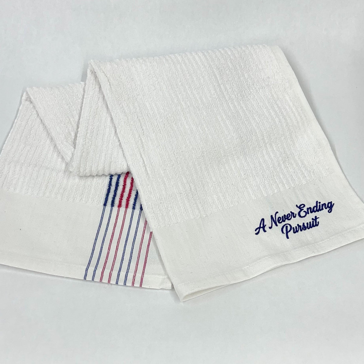 Moment Golf white cotton caddy towel with red and blue stripes and A Never Ending Pursuit embroidery
